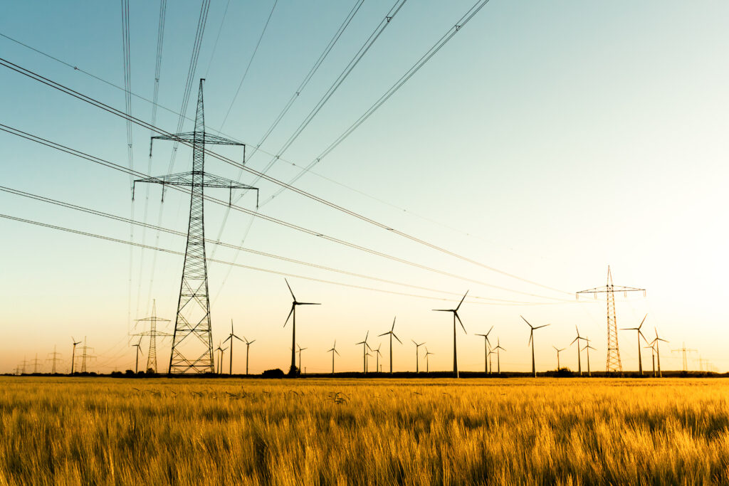 Windkraftanlagen und Freileitungsmast auf einem Feld.