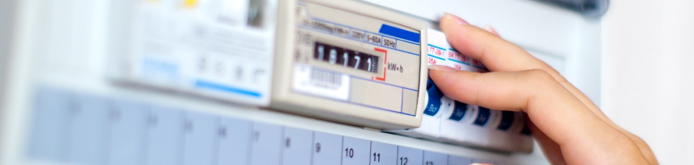Eine Hand greift an einen Stromzähler in einem geöffneten Sicherungskasten.
